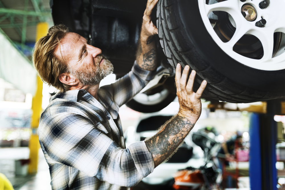 a middle aged man with tattoos inspecting a tire on a vehicle