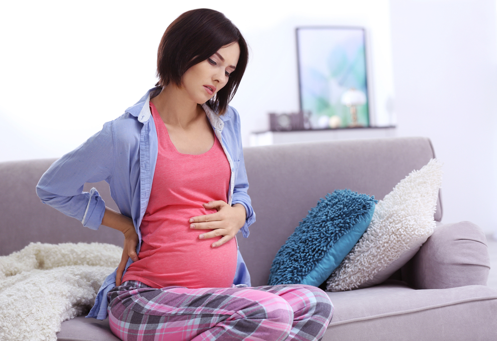 Pregnant woman with back pain sitting on couch