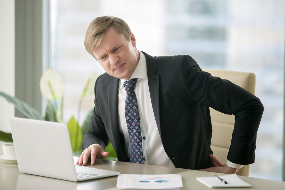 man in a suit in back pain sitting at a desk