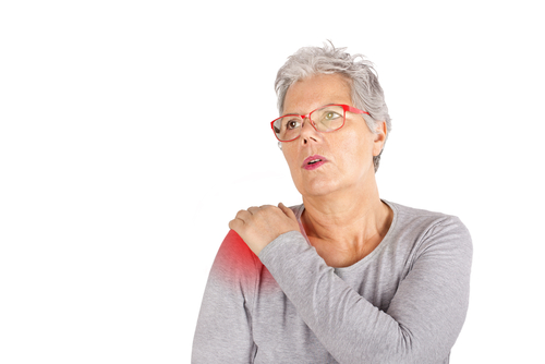 a woman with short, white hair and red glasses grabbing her right shoulder in pain